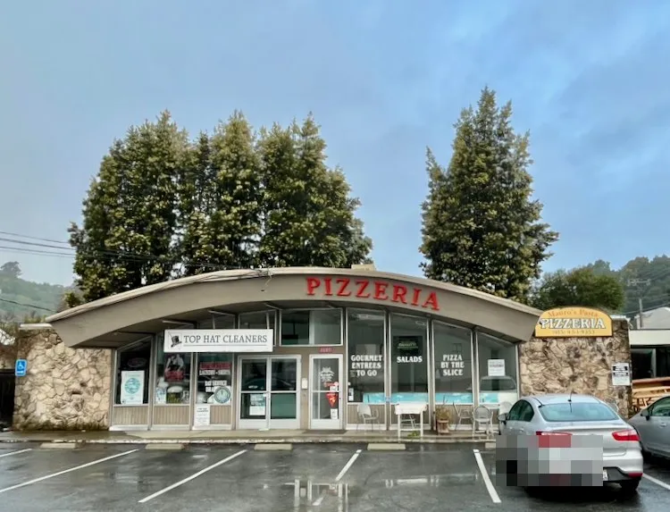 The 1601 Sir Francis Drake building before La Flōr, home to Mauro's Pasta Pizzeria and Top Hat Cleaners under its original curved canopy, on an overcast day.