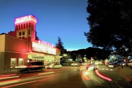 The Fairfax Theatre marquee lit at dusk on Sir Francis Drake Boulevard, cars streaming past on the main street through town.