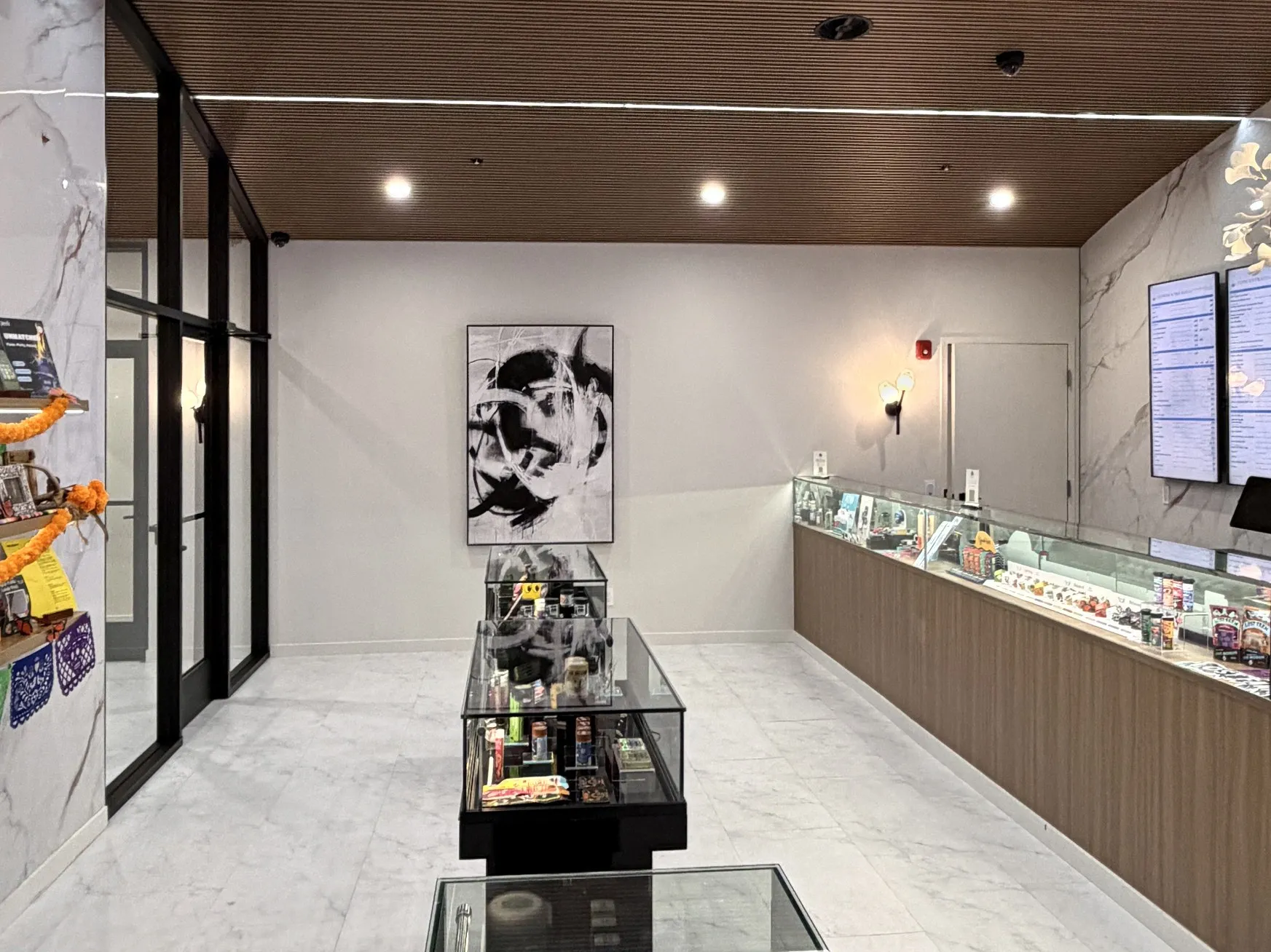 The retail room end to end: marble floor, glass cases down the middle, the long oak counter and the menu screens.