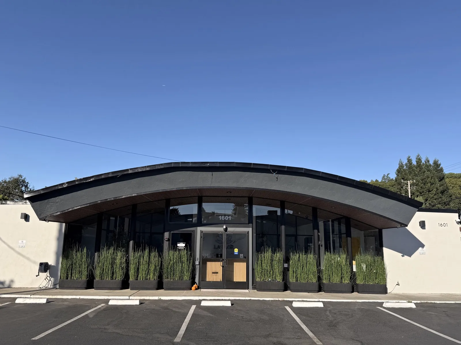 The same building today as La Flōr, seen from the same spot in the parking lot: the curved canopy, the glass front and the planters along the walk.