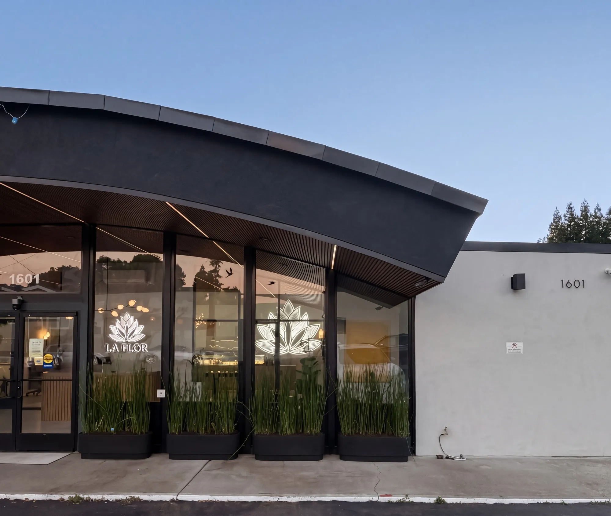 La Flōr at dusk: the dark curved canopy, the glowing lotus in the windows and the round La Flōr sign.